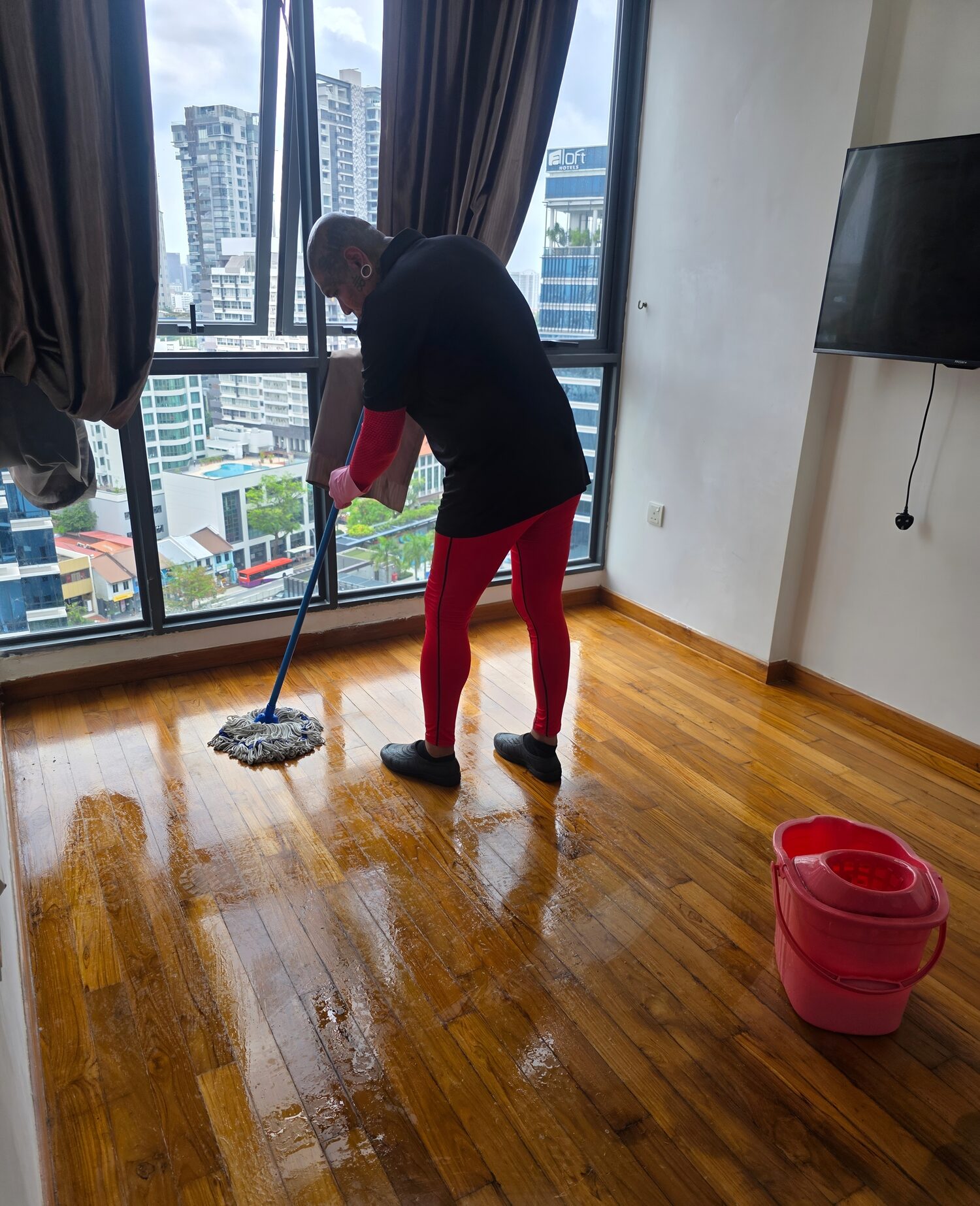 An SFC team member mopping a timber floor in a Singapore high-rise apartment