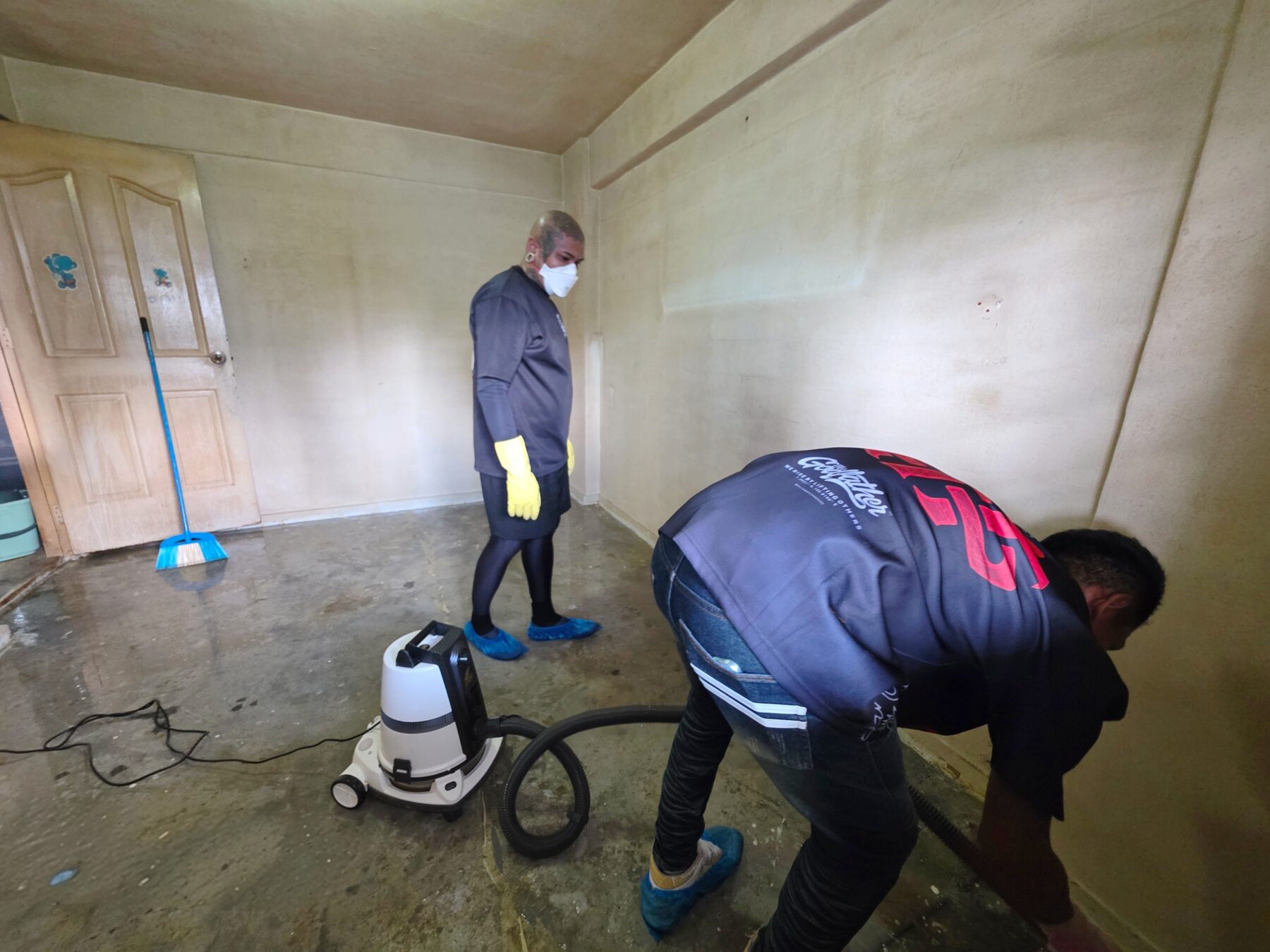 An SFC technician in mask, gloves and shoe covers working a stripped unit while a colleague runs the wet vacuum