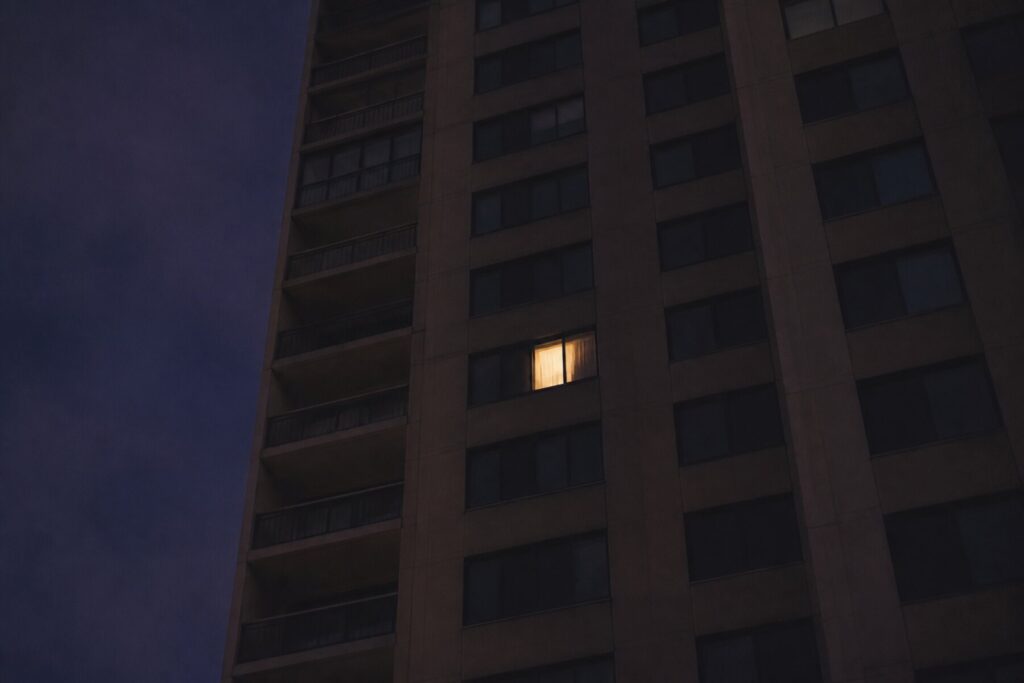 A high-rise residential block at dusk with a single window lit from inside.