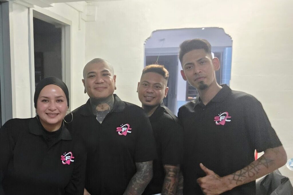 Four members of the SFC team, three men and a woman in a black headscarf, standing together in matching black polo shirts with the SFC logo on the chest.